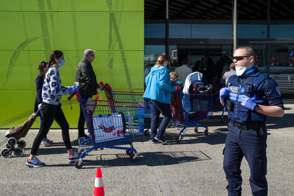 A local policeman with a protective facemask looks on as people wait to enter a supermarket on March 16, 2020, in Illzach, eastern France, while protective measures are taken in France against the spread of the COVID-19. - French President will speak on television at 8:00 (Paris time) on March 16, 2020 to announce new measures to fight the growing coronavirus epidemic, said the Elysee. (Photo by SEBASTIEN BOZON / AFP) (Photo by SEBASTIEN BOZON/AFP via Getty Images)