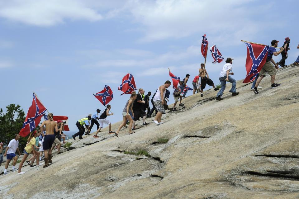 FILE - In this Aug. 1, 2015 file photo, Confederate flag supporters climb Stone Mountain to protest of what they believe is an attack on their Southern heritage during a rally at Stone Mountain Park in Stone Mountain, Ga. The sculpture of Gen. Robert E. Lee, Confederate President Jefferson Davis and Gen. Thomas J. "Stonewall" Jackson on the face of Stone Mountain is America's largest Confederate memorial. (AP Photo/John Amis, File)