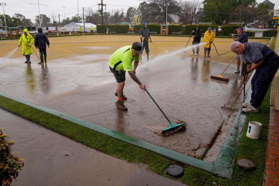 Workers clear mud from a bowling green at Camden, Sydney (AP)