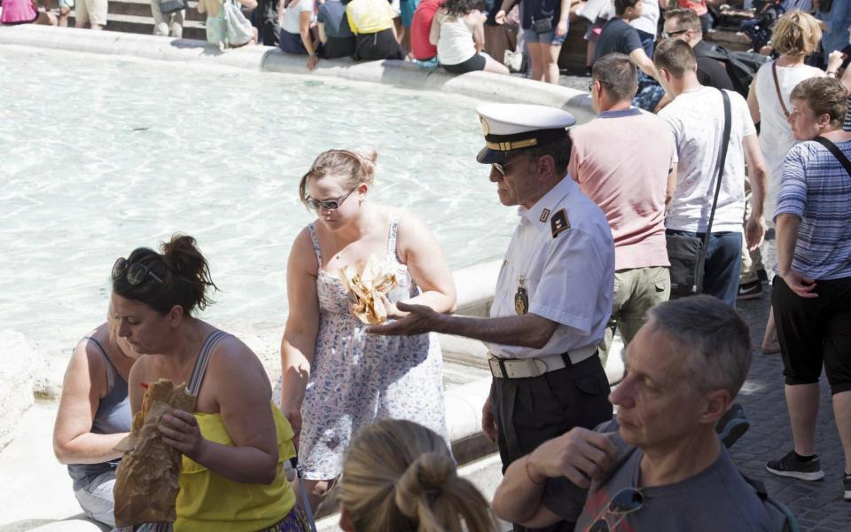 A municipal police officer tells tourists to leave as they were eating on the rim of the Trevi Fountain in Rome - Credit: Ansa via EPA