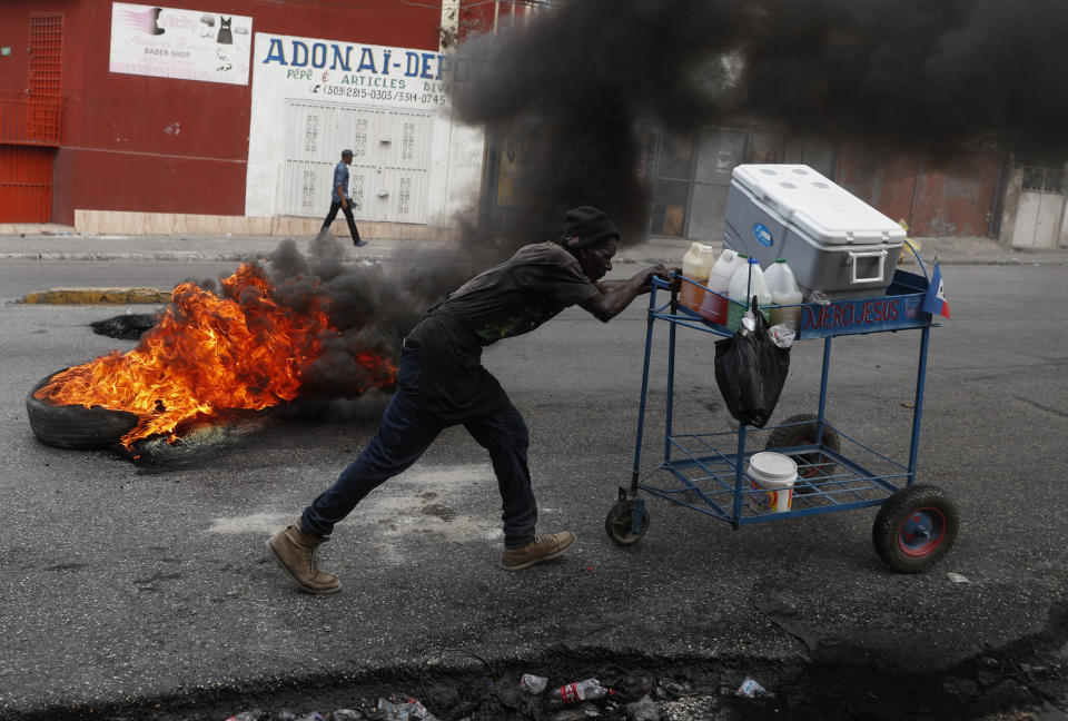 A snow cone vendor pushes his cart past a burning barricade placed by anti-government protesters after President Jovenel Moïse said he would not resign in Port-au-Prince, Haiti, Tuesday, Oct. 15, 2019. The president broke his silence Tuesday and said it would be irresponsible for him to resign amid Haiti's unrest, which has entered a fifth week of deadly protests that have paralyzed the economy and shuttered schools.(AP Photo/Rebecca Blackwell)