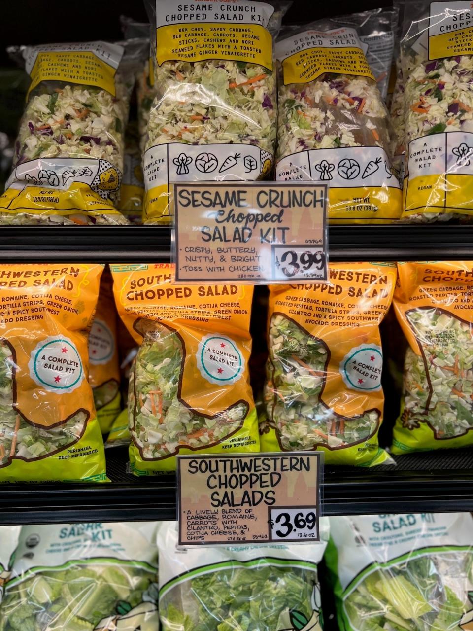 Assorted prepackaged salad kits on grocery store shelf with visible prices and names