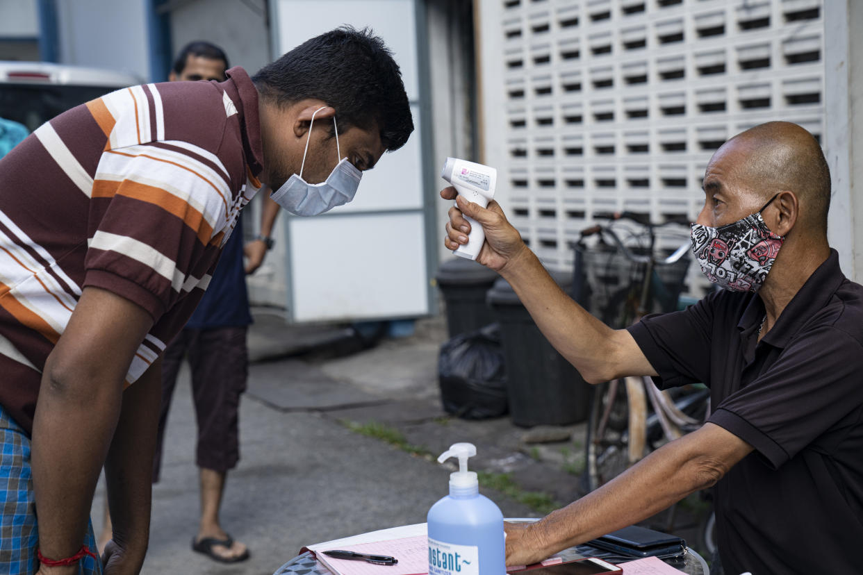 SINGAPORE, SINGAPORE - APRIL 17: A migrant worker wearing protective face mask has his temperature checked by a security guard before leaving a factory-converted dormitory on April 17, 2020 in Singapore. The Coronavirus (COVID-19) pandemic has spread to many countries across the world, claiming over 140,000 lives and infecting more than 2 million people. (Photo by Ore Huiying/Getty Images)