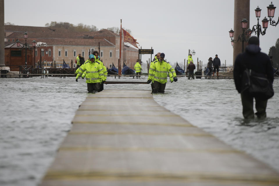 Municipality workers carry wooden boards to make a trestle bridge in a flooded St. Mark's Square at Venice, Italy, Friday, Nov. 15, 2019.The high-water mark hit 187 centimeters (74 inches) late Tuesday, Nov. 12, 2019, meaning more than 85% of the city was flooded. The highest level ever recorded was 194 centimeters (76 inches) during infamous flooding in 1966. (AP Photo/Luca Bruno)