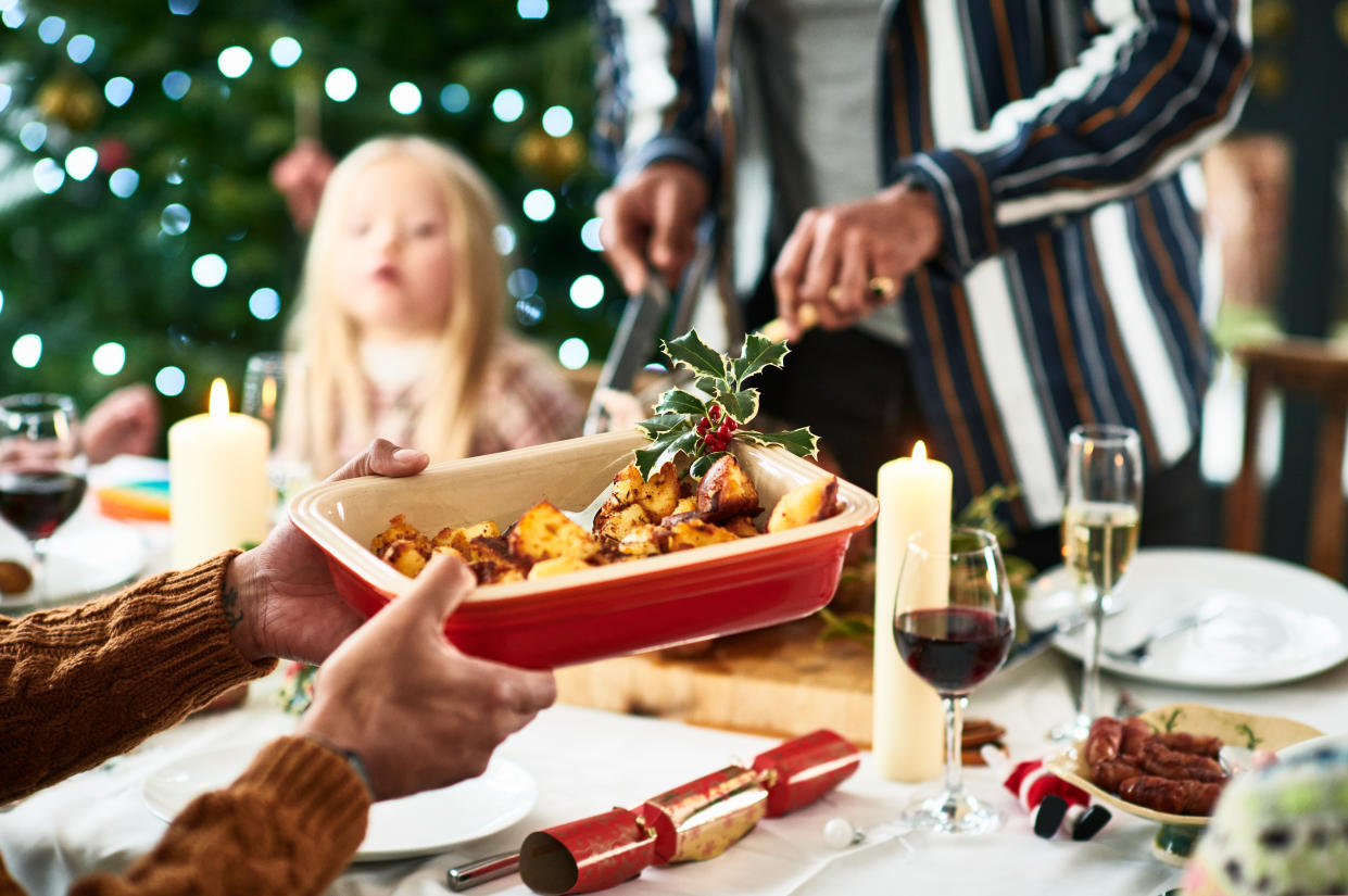 Family Christmas meal with home cooked food being served at dining table, traditional holly with berries garnishing roasted vegetables for gut health, Christmas cracker on table with wine and candles