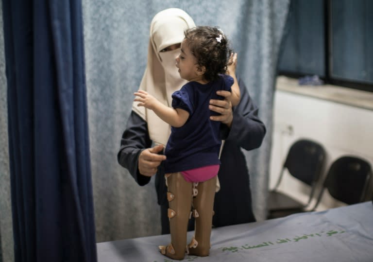 A woman supports her child as she tries to stand in prosthetic legs at Gaza's Artificial Limbs and Polio Centre