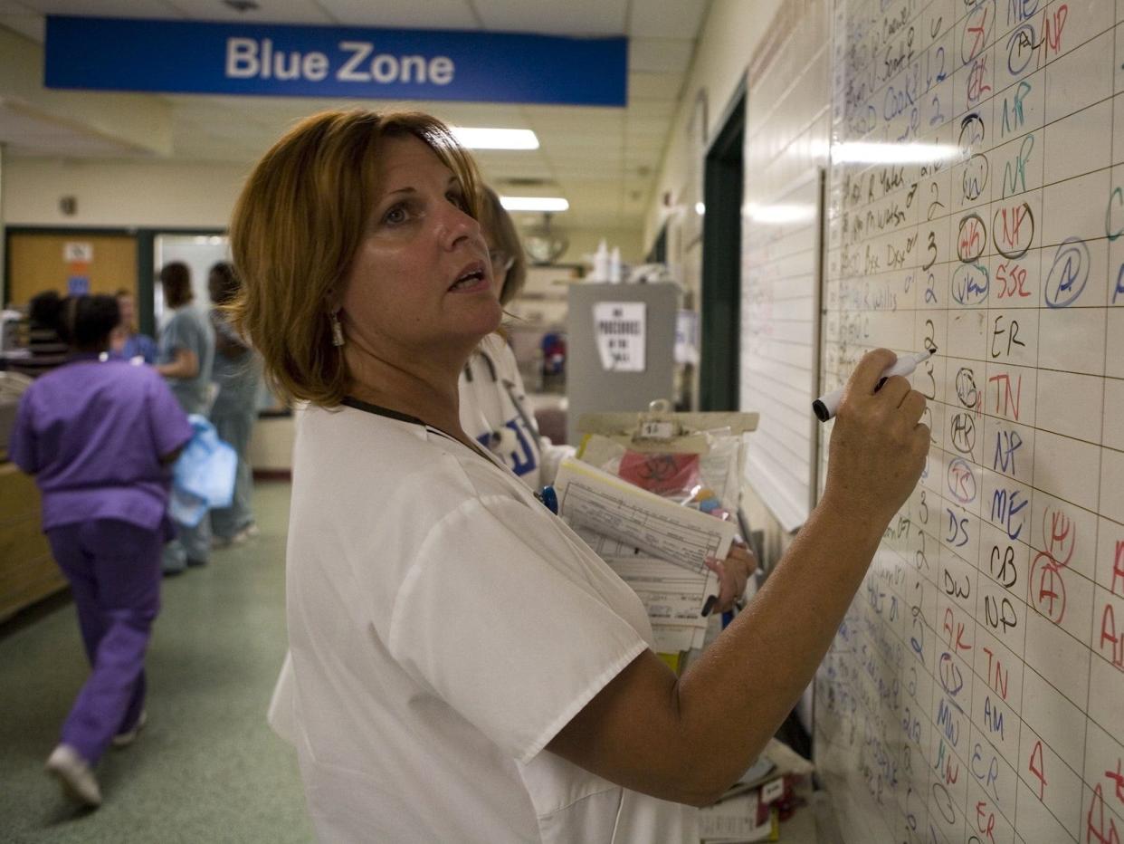 a healthcare worker updating a white board of patients in a crowded ER