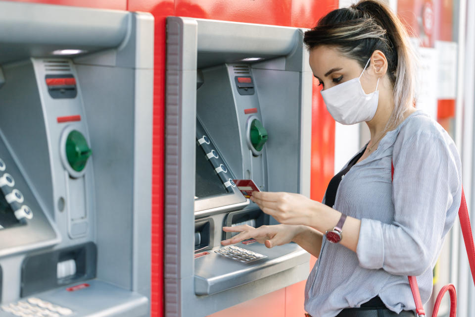 Young woman wearing protective face mask while withdrawing money at ATM