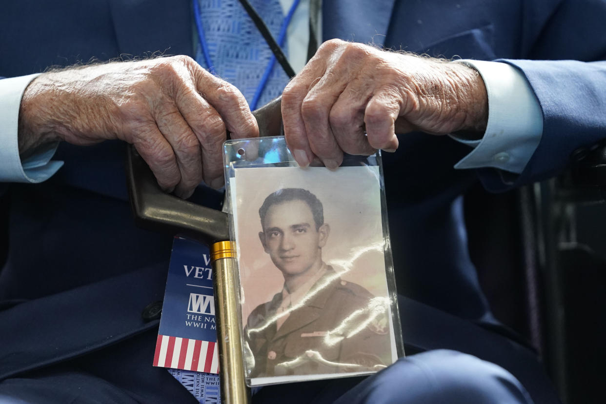 World War II veteran Joseph Eskenazi, who at 104 years and 11 months old is the oldest living veteran to survive the attack on Pearl Harbor, holds a photo of his younger self, at an event celebrating his upcoming 105th birthday at the National World War II Museum in New Orleans, Wednesday, Jan. 11, 2023. (AP Photo/Gerald Herbert)