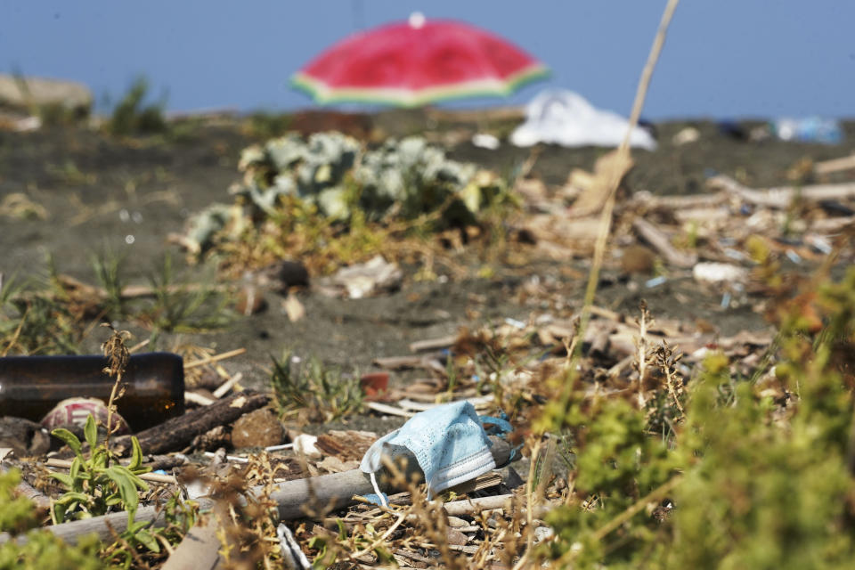 A protective mask is seen among other garbage on a beach at Fiumicino, near Rome, Saturday, Aug. 15, 2020. Italy produced 10% less garbage during its coronavirus lockdown, but environmentalists warn that increased reliance on disposable masks and packaging is imperiling efforts to curb single-use plastics that end up in oceans and seas. (AP Photo/Andrew Medichini)