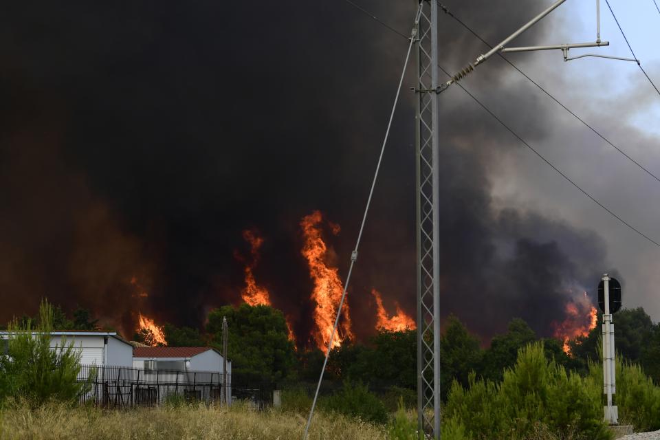 Flames burn near the buildings and railway lines in Tatoi area, northern Athens, Greece, Tuesday, Aug. 3, 2021. Greece Tuesday grappled with the worst heatwave in decades that strained the national power supply and fueled wildfires near Athens and elsewhere in southern Greece. As the heat wave scorching the eastern Mediterranean intensified, temperatures reached 42 degrees Celsius (107.6 Fahrenheit) in parts of the Greek capital. (AP Photo/Michael Varaklas)