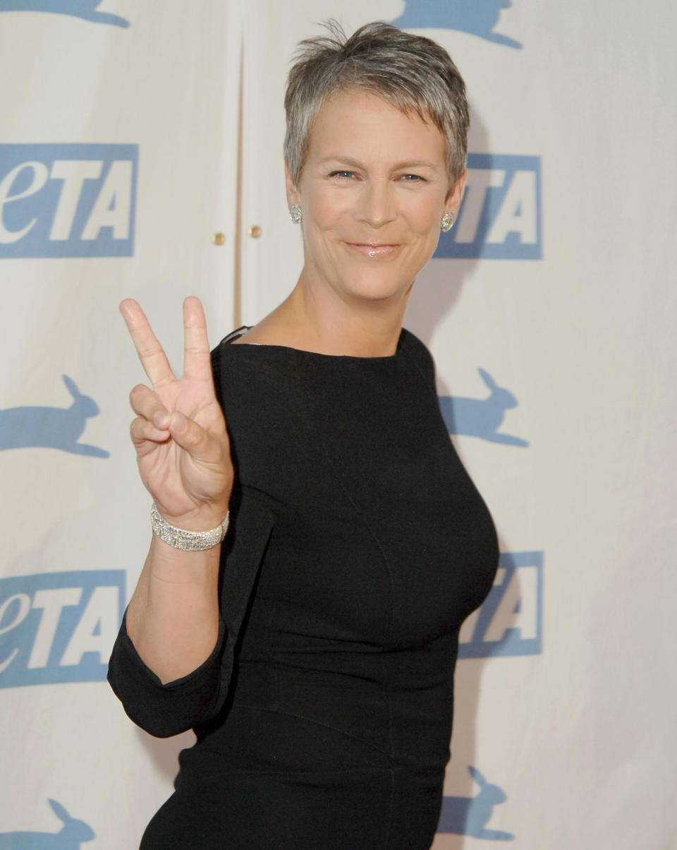 Jamie Lee Curtis poses with a peace sign, wearing a black dress and diamond earrings at an event