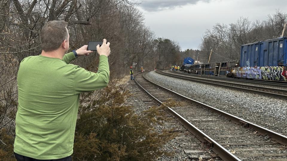 Scott Vacheresse photographs the scene of a freight train derailment, Thursday, March 23, 2023, in Ayer, Mass. No hazardous materials were being hauled, according to the local fire department. Video appeared to show Norfolk Southern engines hauling several railcars that had toppled off the tracks onto their sides. (AP Photo/Rodrique Ngowi)