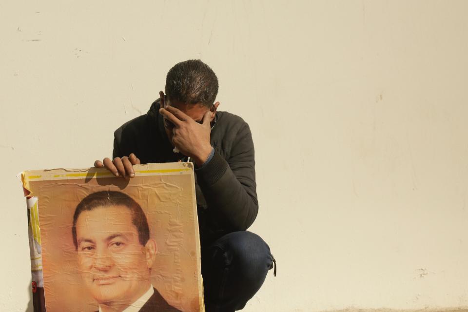 FILE - In this Feb. 26, 2020, file photo, a supporter holds a photo of Egypt's ousted autocratic President Hosni Mubarak as he weeps outside the gate of the mosque ahead of his funeral in New Cairo, Egypt. Mubarak, 91, the Egyptian leader who was the autocratic face of stability in the Middle East for nearly 30 years before being forced from power in an Arab Spring uprising, died Feb. 25. (AP Photo/Maya Alleruzzo, File)