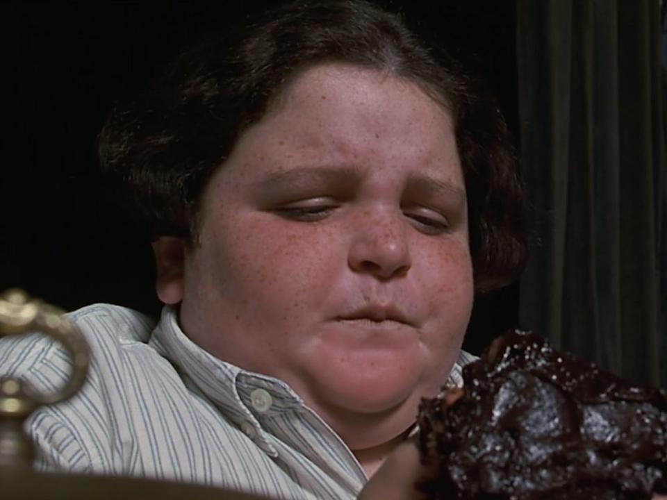 Jimmy Karz as Bruce wearing a green and white striped shirt holding a large piece of chocolate cake