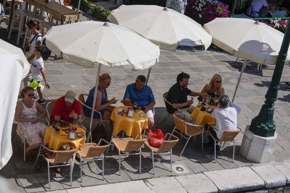 Customers sit at a cafe, in Venice, Italy, Thursday, June 17, 2021. After a 15-month pause in mass international travel, Venetians are contemplating how to welcome visitors back to the picture-postcard canals and Byzantine backdrops without suffering the indignities of crowds clogging its narrow alleyways, day-trippers perched on stoops to imbibe a panino and hordes of selfie-takers straining for a spot on the Rialto Bridge or in front of St. Mark’s Basilica. (AP Photo/Luca Bruno)