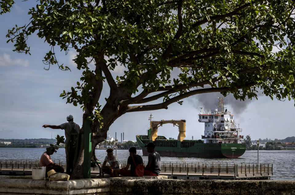 Fishermen sit in the shade as the "Carmita" cargo ship, flying a Panamanian flag, navigates the bay of Havana, Cuba, Thursday, Oct. 22, 2020. Cuba's foreign minister presented the nation's report on the impact of the U.S. embargo over the past year on Thursday. (AP Photo/Ramon Espinosa)