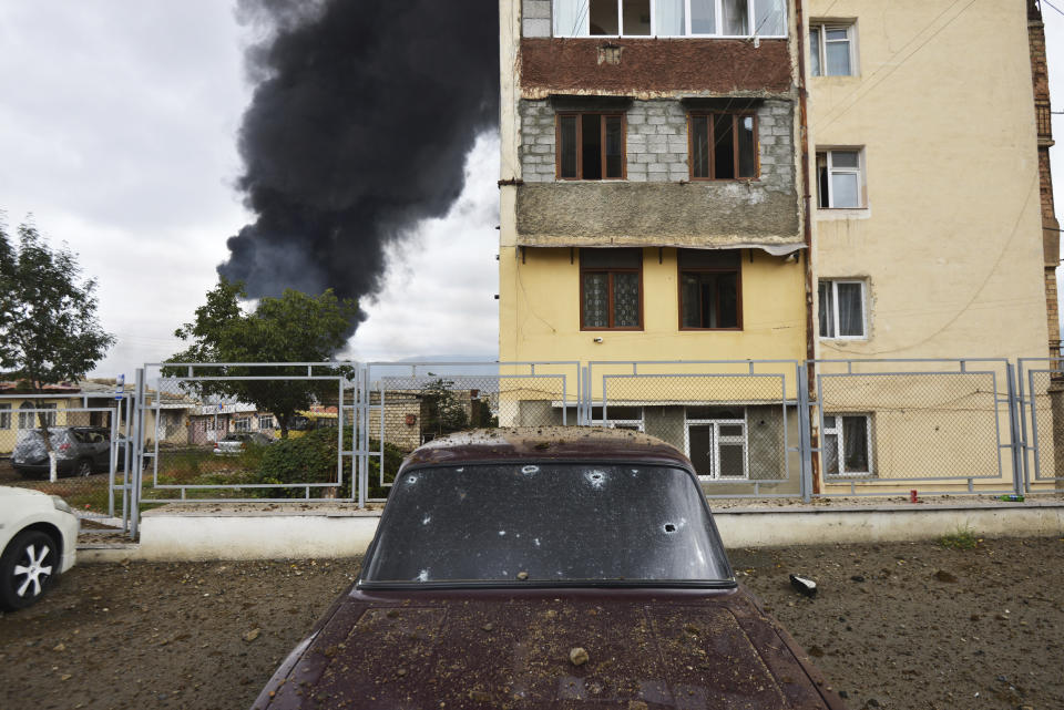 Shrapnel holes in a car as a building burns in the background after shelling by Azerbaijan's artillery during a military conflict in self-proclaimed Republic of Nagorno-Karabakh, Stepanakert, Azerbaijan, Sunday, Oct. 4, 2020. The fighting between Armenian and Azerbaijani forces has continued on Sunday over the separatist territory of Nagorno-Karabakh, with Azerbaijan's second largest city, Ganja, coming under attack. (Karo Sahakyan/ArmGov PAN Photo via AP)