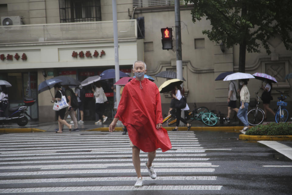 A resident wearing a mask and rain gear crosses the road in Shanghai, China, Tuesday, Sept. 14, 2021. Flights and train service were being canceled in Shanghai, China's largest city, as Typhoon Chanthu moved up the mainland coast Monday after bringing heavy rain and wind to Taiwan. (AP Photo/Chen Si)