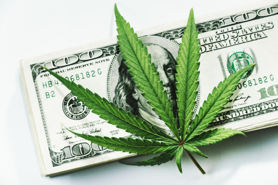 A cannabis leaf on top of a pile of one hundred dollar bills.