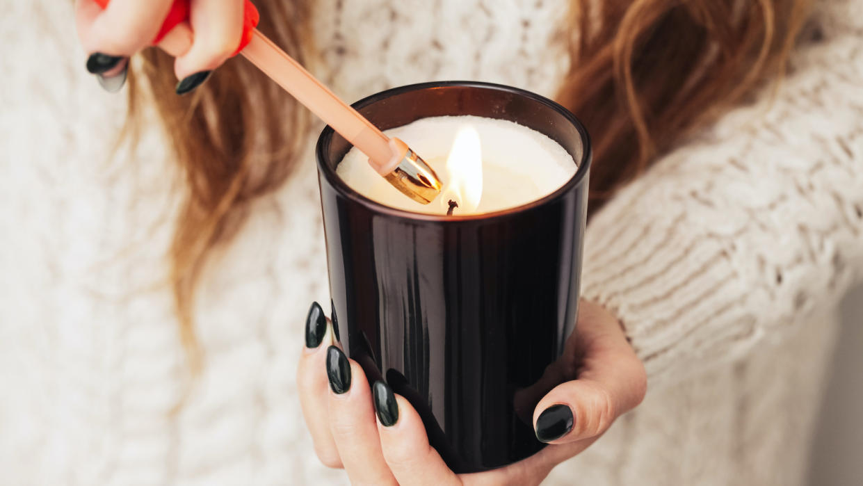  A woman with long hair, whose face you can't see, in a white sweater with black nail polish lighting a candle with a lighter. 