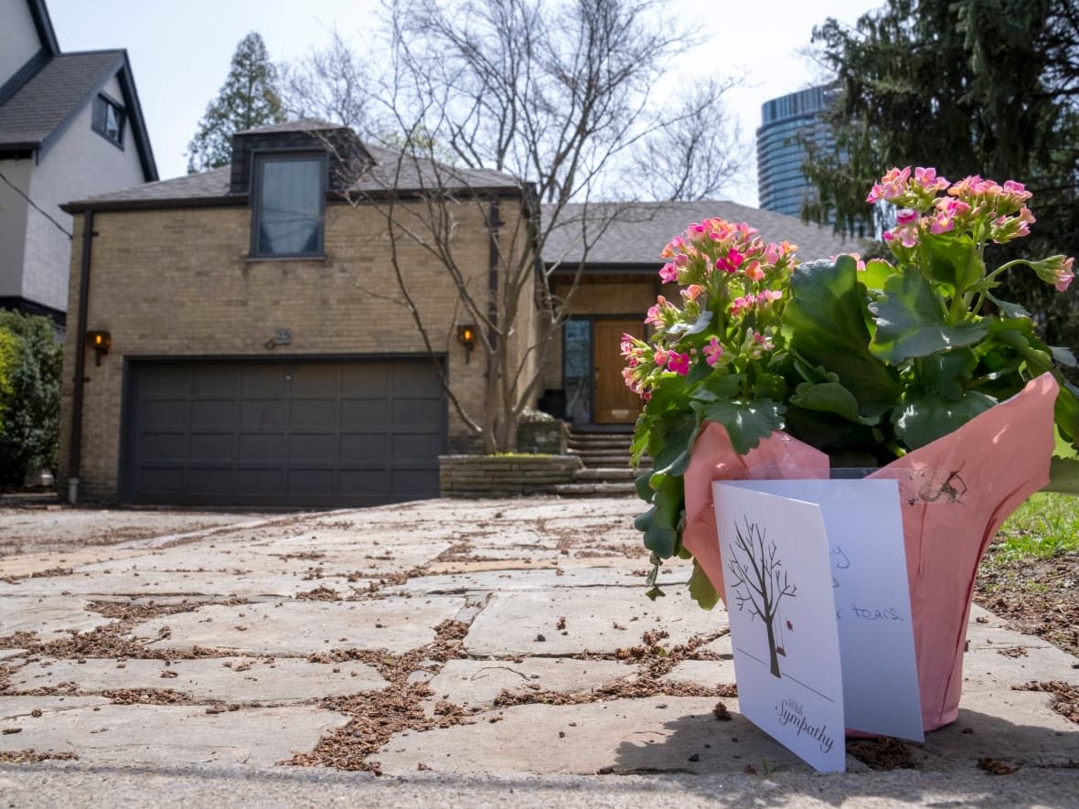 Flowers and a card sit on the driveway of the Rosedale house where the wrapped body of a young girl was found in a construction site dumpster bin in Toronto. (Frank Gunn/Canadian Press - image credit)