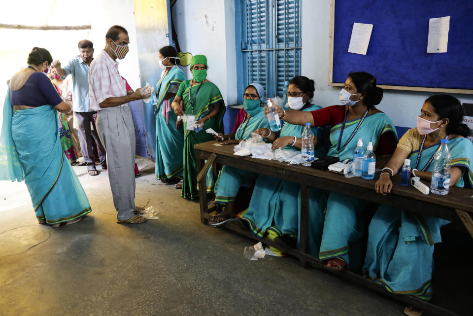 Volunteers offer gloves and sanitizers to voters at the entrance of a polling station during the fourth phase of West Bengal state elections in Kolkata , India, Saturday, April 10, 2021. (AP Photo/Bikas Das)