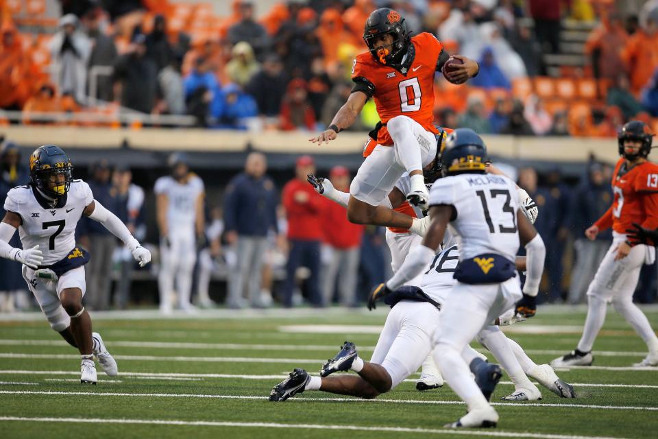 Oklahoma State running back Ollie Gordon (0) leaps over West Virginia defensive back Caleb Coleman (16) during a 24-19 loss Saturday.