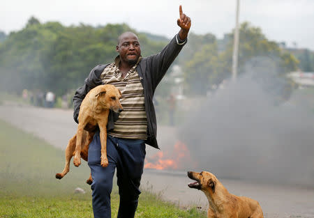 A protester gestures as he holds a dog before a burning barricade during protests in Harare, Zimbabwe, January 15, 2019. REUTERS/Philimon Bulawayo