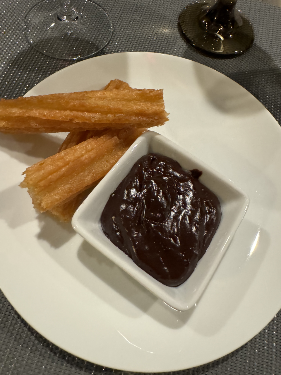 A plate of churros and a bowl of thick chocolate sauce on a white dish, ready for dipping