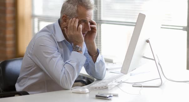 Senior businessman sitting at  computer holding hands to head