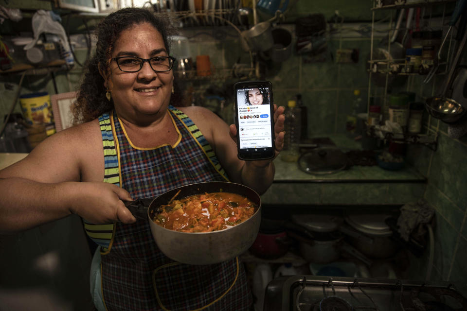 Contributor Yuliet Colon poses for a photo holding a pot of her creation, “Cuban-style pisto manchego," and her phone that displays the Facebook page, “Recipes from the Heart,” in her home in Havana, Cuba, Friday, April 2, 2021. Colon, a 39-year-old mother of two, found for herself a solution that combines ingenuity with the innovative use of the Internet and became a contributor to “Recipes from the Heart,” with tips, ideas and tricks to get ahead with items that are actually available at the market. (AP Photo/Ramon Espinosa)