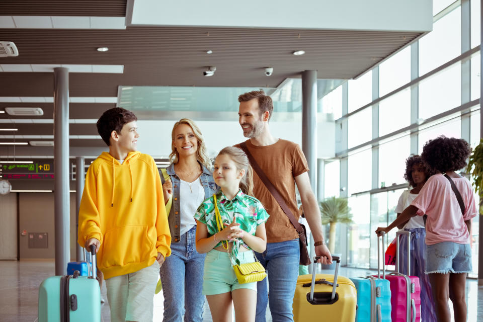 Parents with children standing at airport, holding luggage.