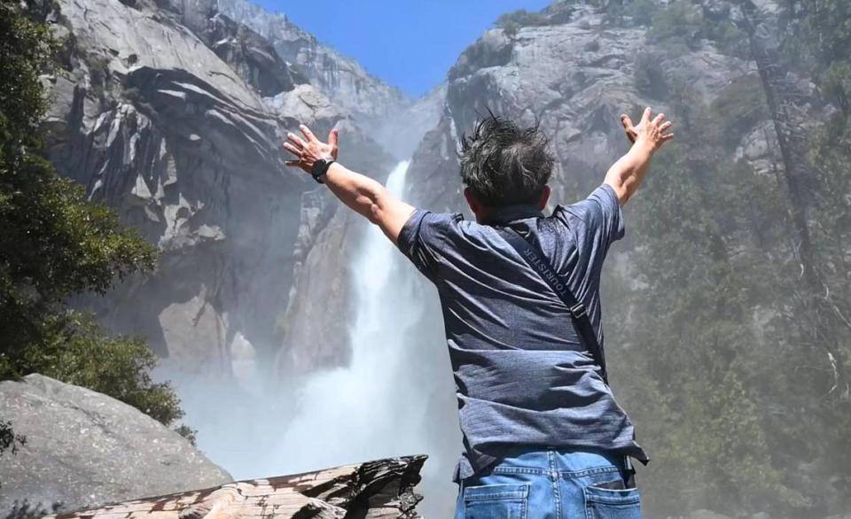 An unidentified park visitor raises his arms as the freezing spray from Lower Yosemite Fall drenches visitors Friday, April 28, 2023 in Yosemite Valley.