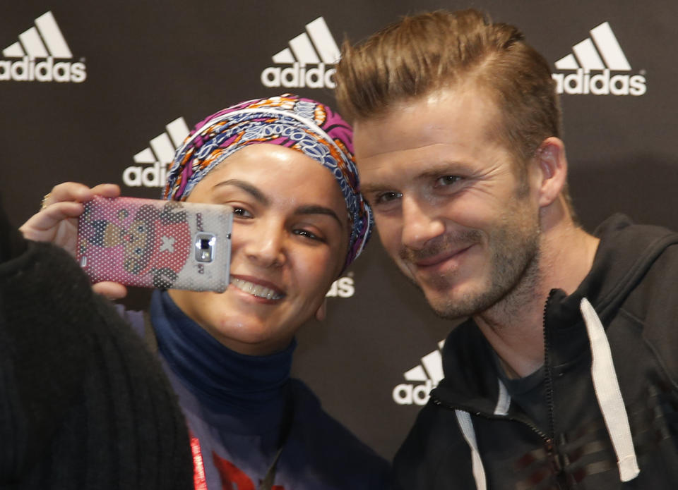 File - In this Thursday, Feb. 28, 2013, file photo Paris Saint Germain's David Beckham poses for a photograph with unidentified fan during a media event, in a sports store, on the Champs Elysees Avenue, in Paris. Selfie" the smartphone self-portrait has been declared word of the year for 2013 by Britain's Oxford University Press. (AP Photo/Francois Mori, File)