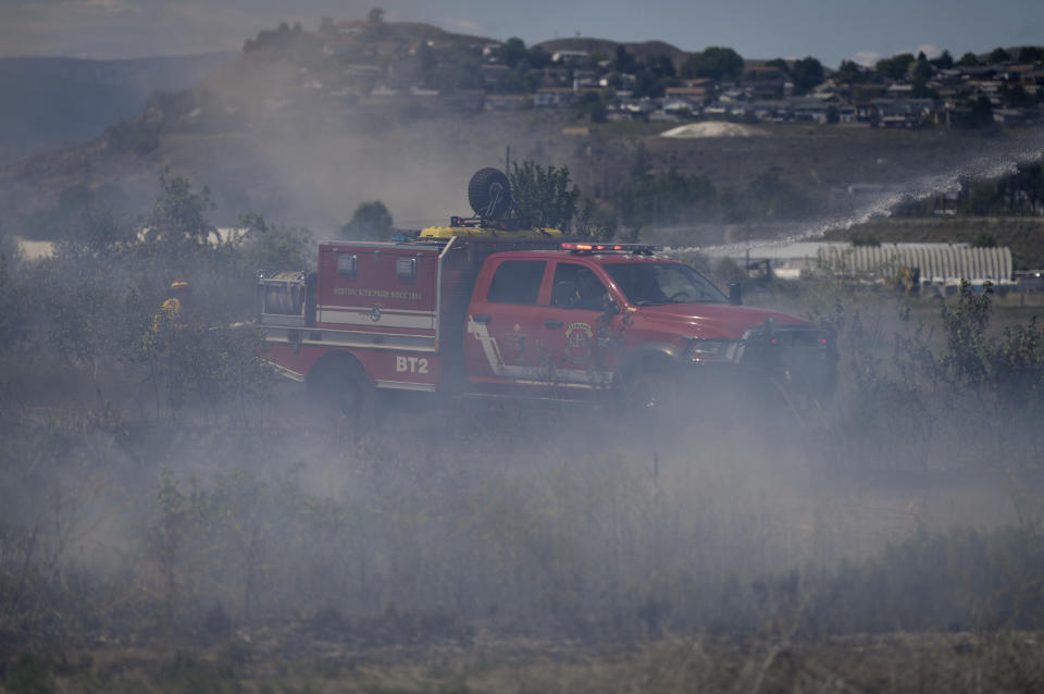 Firefighters battle a grass fire burning on an acreage behind a residential property in Kamloops, British Columbia, Monday, June 5, 2023. No structures were damaged but firefighters had to deal with extremely windy conditions while putting out the blaze. (Darryl Dyck/The Canadian Press via AP)