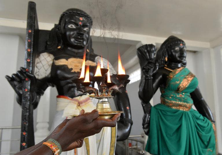 A Hindu priest holds a lit coconut oil lamp in front of statues of Prince Vijaya and demon Princess Kuveni (R) at the Sri Subramaniam temple in Matara on March 7, 2014