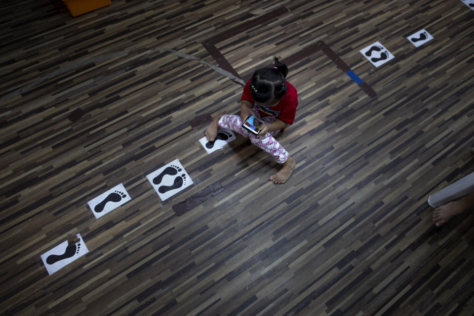 Phatramon Thongthad, a daughter of a teacher of Makkasan preschool, plays with her mobile phone on a floor marked with physical distancing guidelines at the preschool in Bangkok, Thailand, Wednesday, June 24, 2020. The teachers, many of whom are from the community, are eager to have the children back in the classroom but recognize the challenges posed by social distancing active preschoolers in a compact facility in this densely populated community. (AP Photo/Gemunu Amarasinghe)