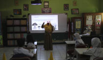 An Indonesian teacher wears a mask and face shield as a precaution against the new coronavirus as she teaches at a class in Bekasi on the outskirts of Jakarta, Indonesia, Monday, Aug. 3, 2020. (AP Photo/Achmad Ibrahim)