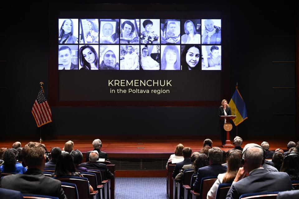 The faces of Ukrainian civilian victims of Russian attachs are displayed on a screen behind Olena Zelenska.