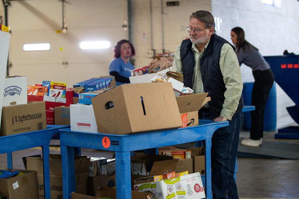 U.S. Senator Gary Peters moves a cart full of donated food items after it was being weighted at the Lighthouse Emergency Services warehouse in Pontiac on Tuesday, Nov. 22, 2022.