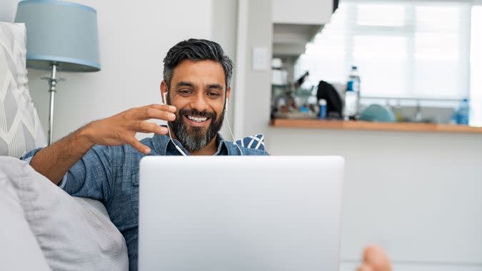 Happy mature man relaxing on couch while video calling using laptop at home.