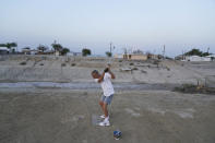 Greg Shank hits golf balls onto a dried up boating dock near his home in Salton City, Calif., Wednesday, July 14, 2021. Shank used to sail a boat on the canals near his property, which have since dried up. Increasing demand for electric vehicles has shifted investments into high gear to extract lithium, critical to rechargeable batteries, from geothermal wastewater around the rapidly shrinking body of water. But decades of economic stagnation and environmental ruin have left some nearby residents indifferent or wary. (AP Photo/Marcio Jose Sanchez)