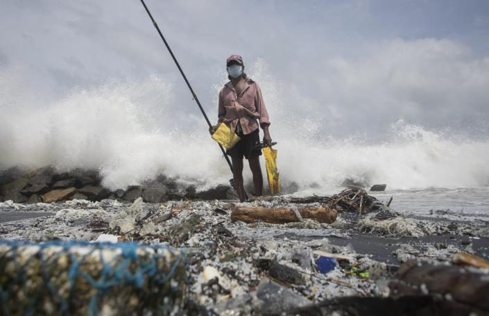 Sri Lankan man, Kindston Jayalath fishes on a polluted beach filled with plastic pellets washed ashore from the fire-damaged container ship MV X-Press Pearl in Kapungoda, on the out skirts of Colombo, Sri Lanka, Friday, June 4, 2021. Authorities were trying to head off a potential environmental disaster as the Singapore flagged ship that had been carrying chemicals was sinking off of the country's main port. (AP Photo/Eranga Jayawardena)