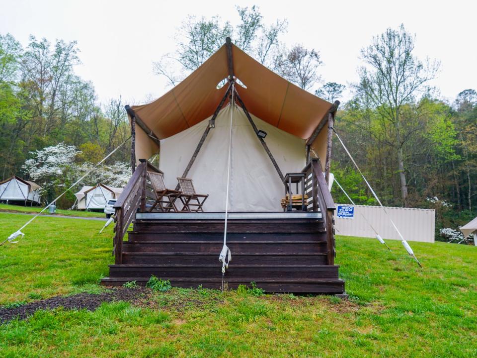 A large tent sitting at the top of a staircase with grass beneath it and trees and other tents behind