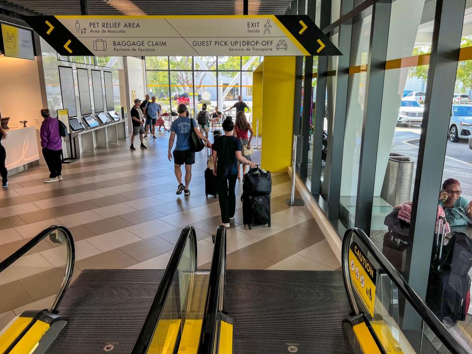 A escalator is shown at the West Palm Beach Brightline station. Passengers are seen in the busy station.