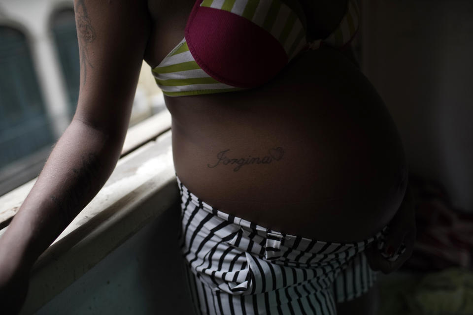 Actress Kelly Regina da Silva, whose pregnant belly is tattooed with her mother’s name, leans against the window ledge of the building where she lives in one of the city center’s squats, in Rio de Janeiro, Brazil, Tuesday, March 16, 2021. Da Silva whose acting career came to an abrupt end due to the pandemic, now works at a nearby supermarket’s deli counter. “I’m scared,” said da Silva acknowledging the risks she is taking by exposing herself to the virus, “But I have to support myself.” (AP Photo/Silvia Izquierdo)