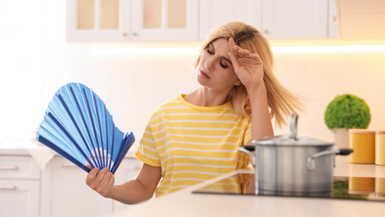  A woman who is overly hot in a kitchen fanning herself 