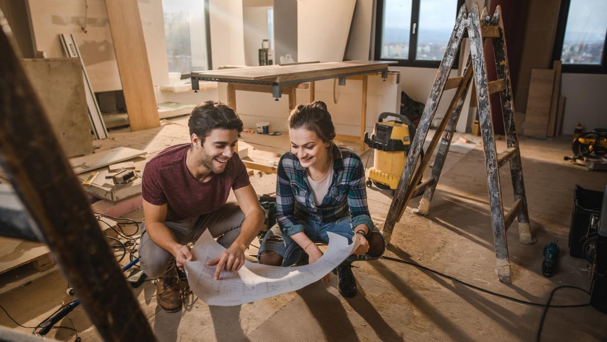 Young happy couple examining blueprints while being on construction site in their apartment.