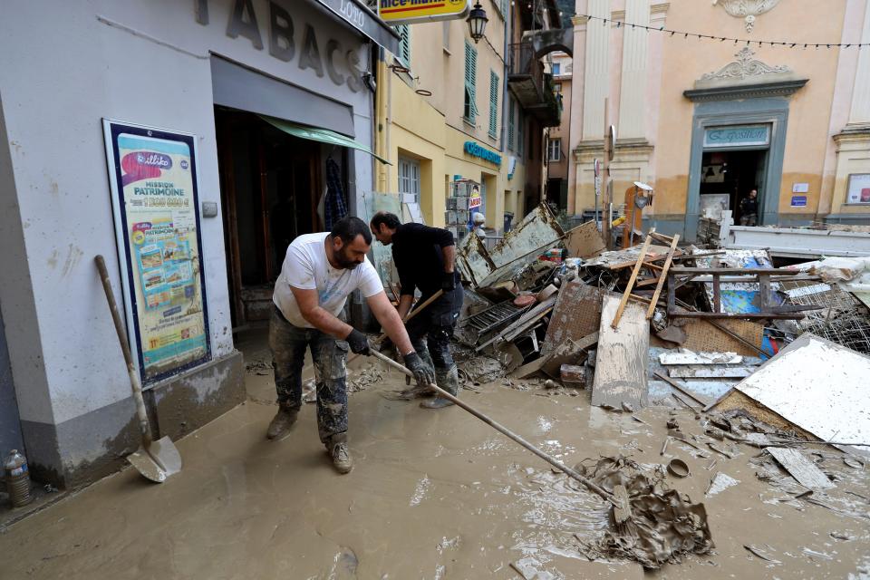 Men bail mud outside a shop.